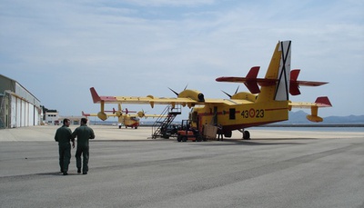 Un piloto y un mecánico de vuelo se dirigen a su hidroavión en la plataforma del aeródromo de Pollensa mientras el personal de mantenimiento carga material en el otro